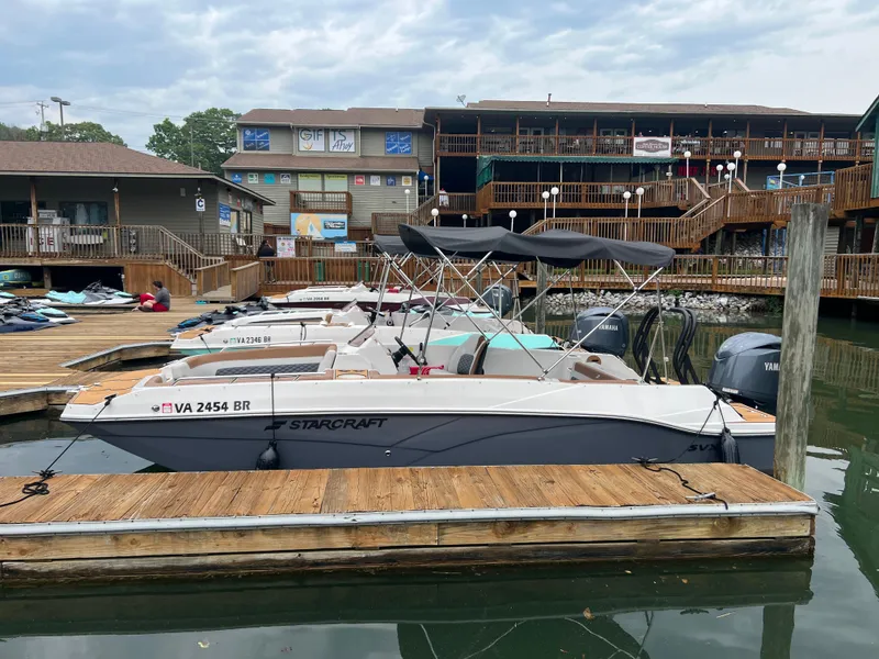 Slide: The Image of 2025 Starcraft SVX 211 OB boat docked at a marina with wooden buildings in the background. - 2