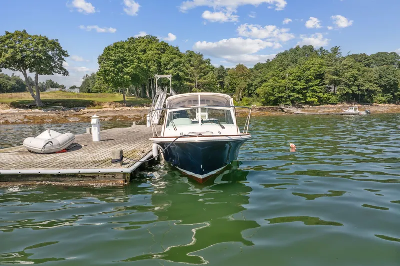 Slide: The Image of 2015 Hunt Yachts 25 Harrier docked by a scenic shoreline with trees and blue sky. - 18