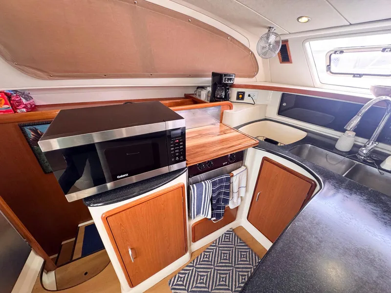 Slide: The Image of Compact kitchen in a 2007 Leopard 43 yacht with microwave, sink, and wooden cabinets. - 22