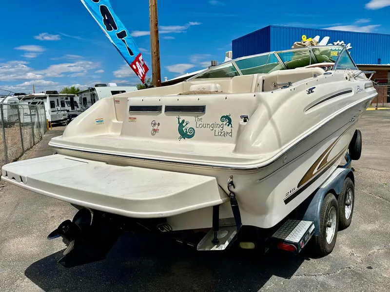 Slide: The Image of 2000 Sea Ray 215 Express Cruiser on trailer, parked outdoors under clear blue sky. - 2