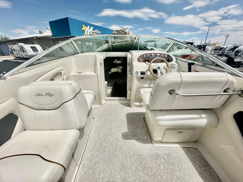 Slide: The Image of 2000 Sea Ray 215 Express Cruiser interior with white seating and dashboard, parked outdoors. - 8