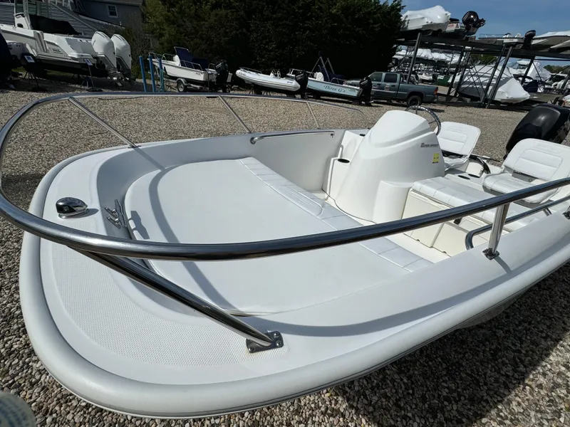 Slide: The Image of 2016 Boston Whaler 150 Super Sport boat on gravel lot, showcasing sleek design and seating. - 8