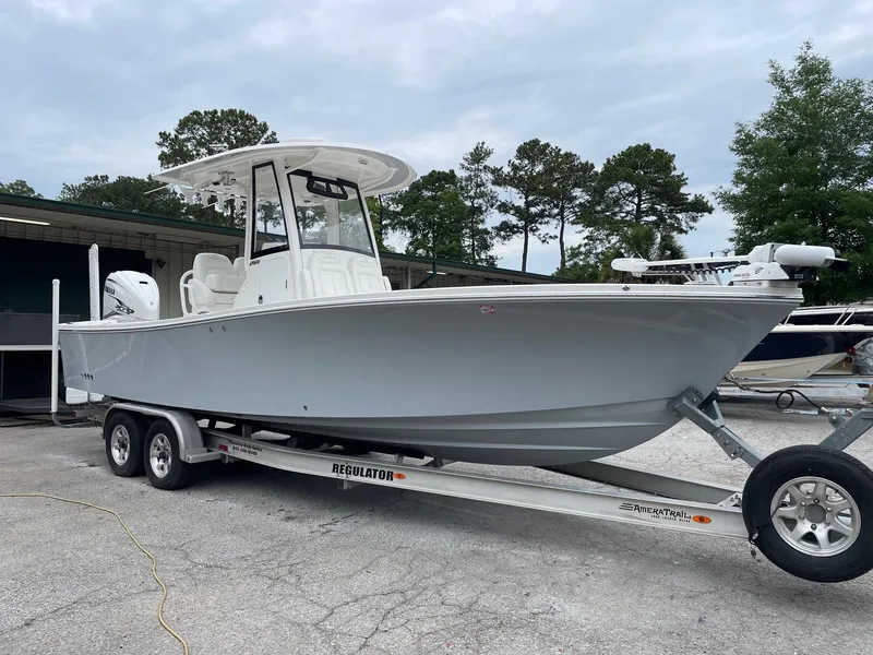 Slide: The Image of 2021 Regulator 26XO boat on trailer, parked outdoors, with trees in the background. - 2