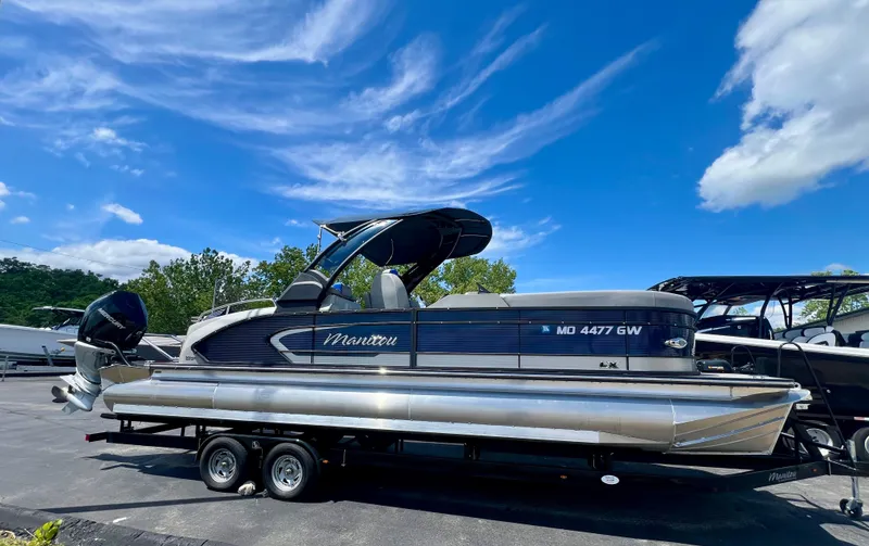 Slide: The Image of 2022 Manitou 25 LX SHP DE pontoon boat on trailer under blue sky. - 0