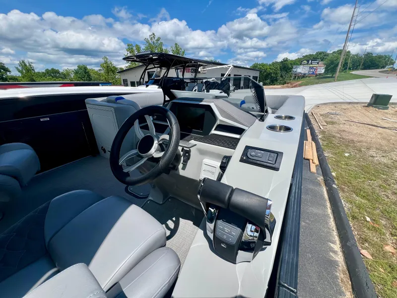 Slide: The Image of 2022 Manitou 25 LX SHP DE boat interior with steering wheel and controls, parked outdoors. - 11