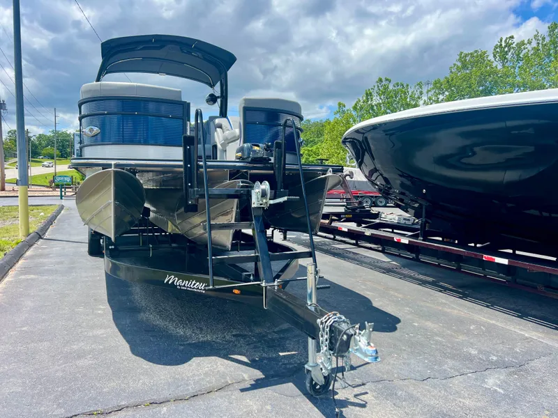 Slide: The Image of 2022 Manitou 25 LX SHP DE pontoon boat on trailer, parked outdoors under cloudy sky. - 2