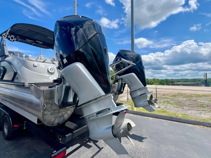 Slide: The Image of 2022 Manitou 25 LX SHP DE pontoon boat with dual outboard motors on a trailer. - 26
