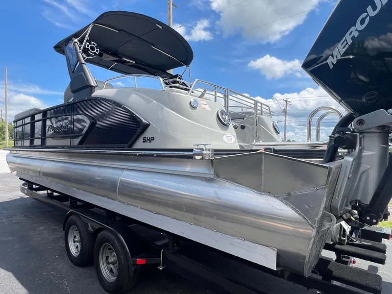 Slide: The Image of 2022 Manitou 25 LX SHP DE pontoon boat on trailer, under blue sky. - 3