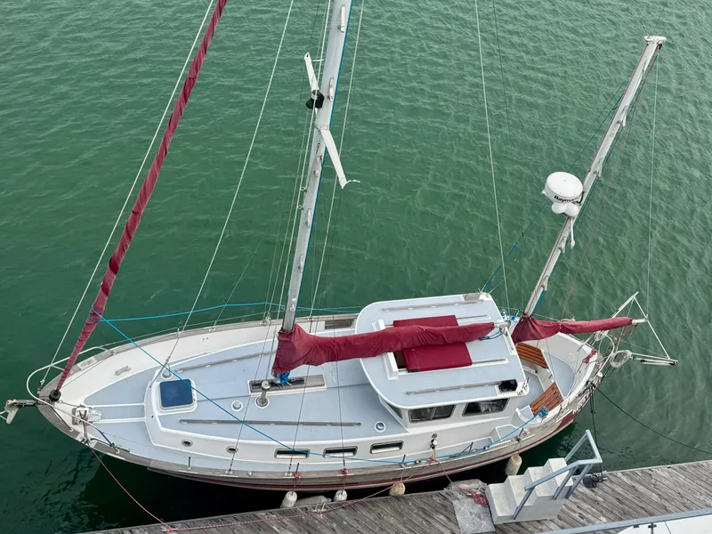 Slide: The Image of 1985 Fisher 34 Pilothouse Ketch docked, featuring red sails and a white hull. - 2