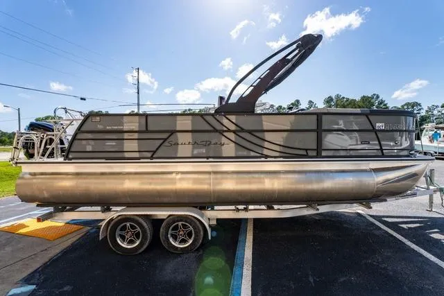Slide: The Image of 2024 South Bay S224 UL 3.0 pontoon boat on trailer, parked outdoors under blue sky. - 6