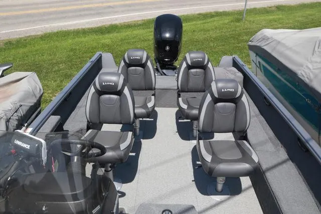 Slide: The Image of 2018 Lund 1875 Impact SC boat interior with four seats and motor, parked on grass. - 9
