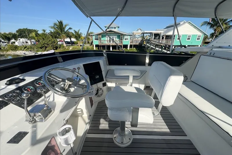 Slide: The Image of 1994 President 445 Sundeck yacht helm with white seating and controls, docked near colorful houses. - 42