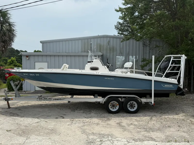 Slide: The Image of 2011 Boston Whaler 230 Dauntless boat on trailer, parked outdoors near a metal building. - 5