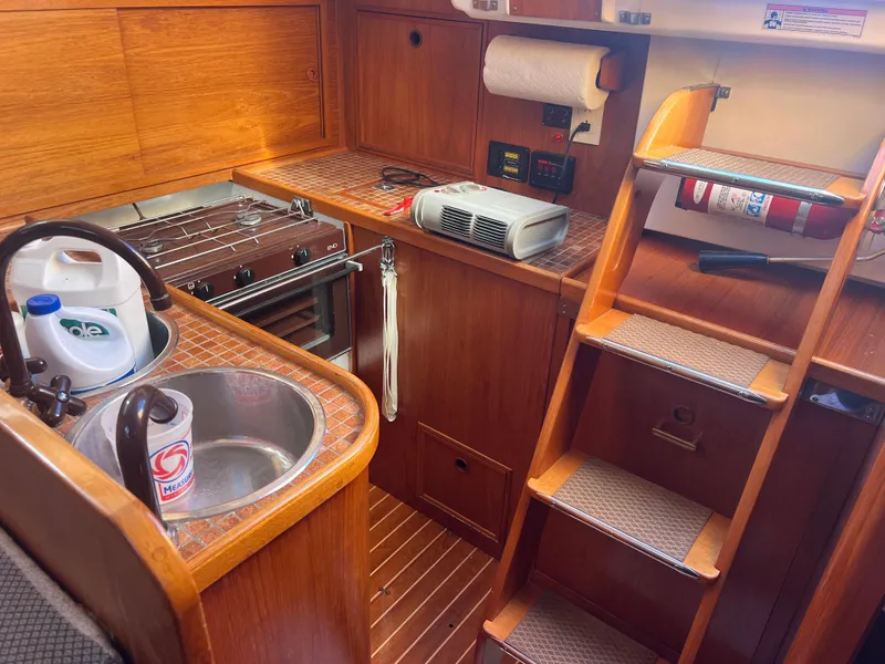 Slide: The Image of 1985 Wauquiez Pretorian Sloop interior with wooden cabinetry, compact kitchen, and stairs. - 24
