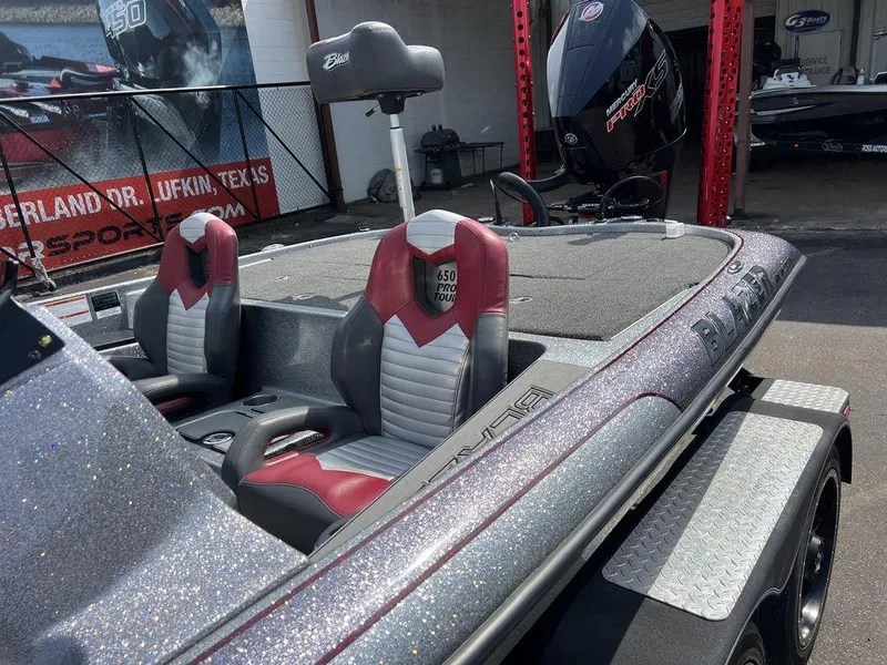 Slide: The Image of 2022 Blazer 650 Pro Tour boat with red and gray seats, parked outdoors. - 24