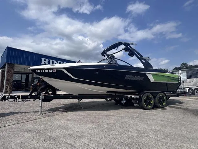 Slide: The Image of 2018 Malibu 24 MXZ boat on trailer, black and green design, parked outside dealership. - 5
