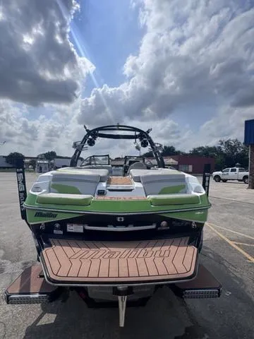 Slide: The Image of 2018 Malibu 24 MXZ boat with green accents, parked outdoors under a cloudy sky. - 7