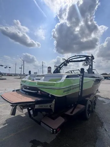 Slide: The Image of 2018 Malibu 24 MXZ boat with green accents on a trailer under a cloudy sky. - 9