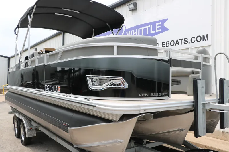 Slide: The Image of 2023 Avalon Venture 2385 RF pontoon boat on trailer, black exterior, docked at dealership. - 11