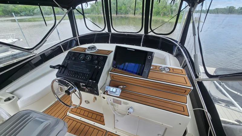 Slide: The Image of 1995 Silverton 41 Convertible yacht helm with modern controls and wood accents, overlooking serene water. - 13