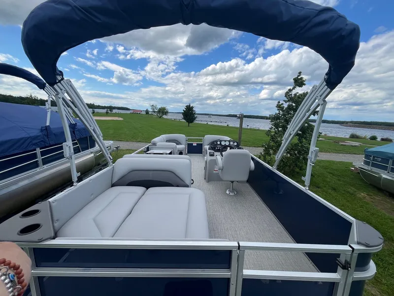 Slide: The Image of 2025 Landau Island Breeze 232 Cruise pontoon boat with canopy, docked by a scenic lake. - 2