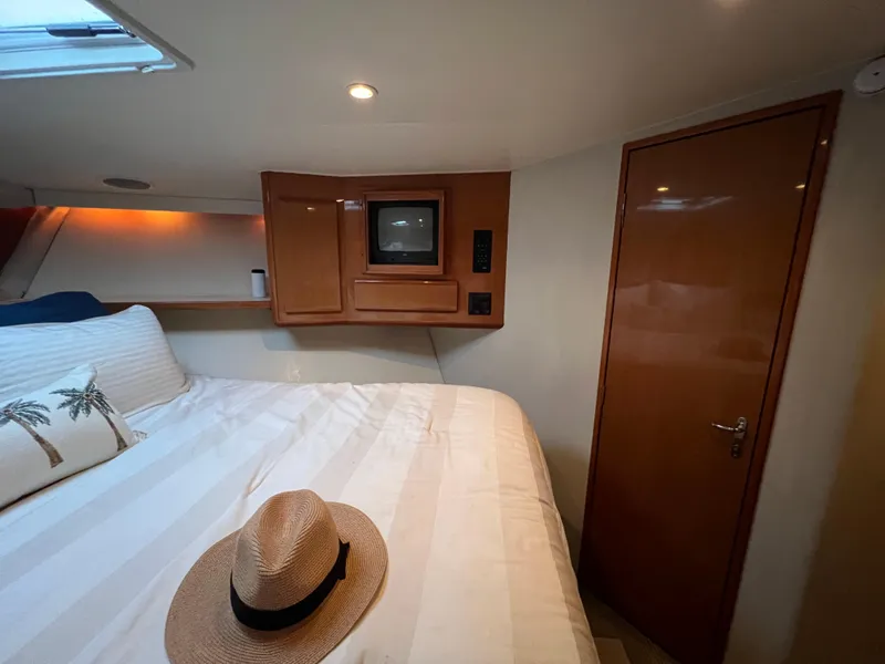Slide: The Image of Cozy bedroom in 2000 Viking 58 Enclosed Bridge yacht with TV and straw hat on bed. - 24