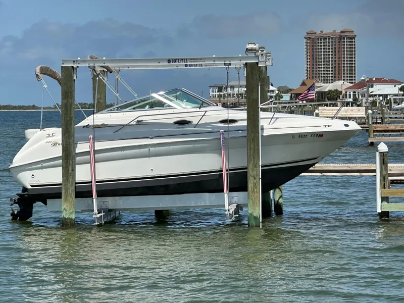 The Image of 1998 Sea Ray 240 Sundancer boat on lift, waterfront view with buildings in background. - 0