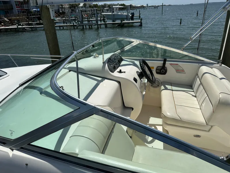 Slide: The Image of 1998 Sea Ray 240 Sundancer boat interior with steering wheel and seating, docked by the water. - 5
