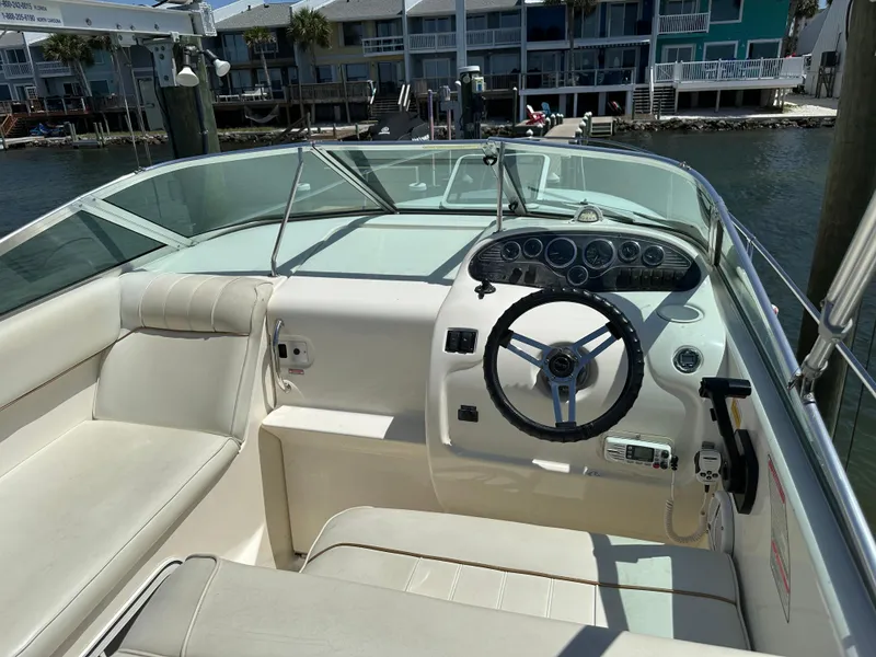 Slide: The Image of 1998 Sea Ray 240 Sundancer boat interior with steering wheel and seating, docked near waterfront homes. - 9