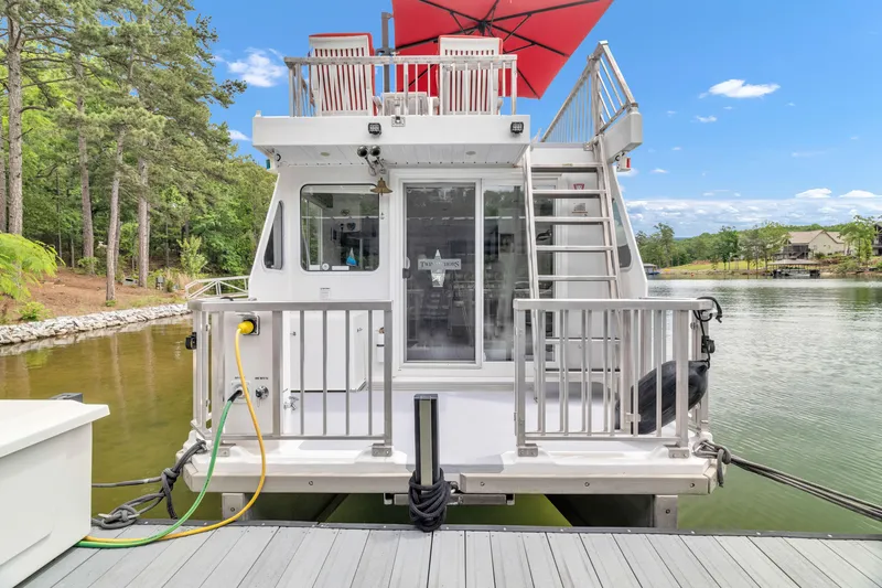Slide: The Image of 2016 Twin Anchors 3010 houseboat docked on a serene lake with red umbrella. - 17