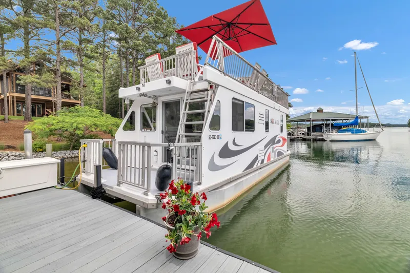 Slide: The Image of Houseboat docked on a lake, Twin Anchors 3010, 2016 model, with red umbrella and floral decor. - 18