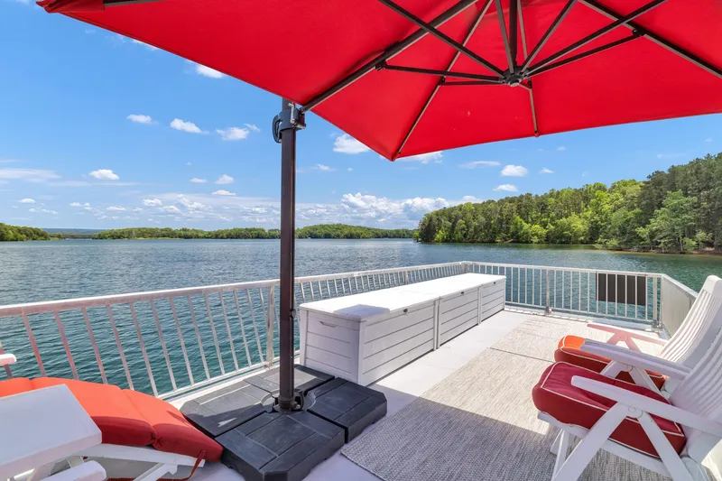 Slide: The Image of Houseboat deck with red umbrella, white seating, and scenic lake view. Twin Anchors 3010, 2016 model. - 23