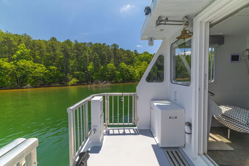 Slide: The Image of Houseboat deck view on a serene lake, surrounded by lush green forest, under a clear blue sky. - 48