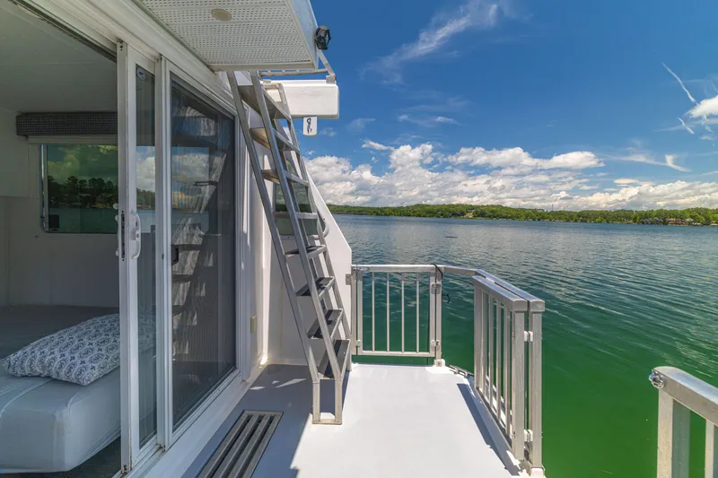 Slide: The Image of Houseboat deck with ladder, overlooking serene lake under a clear blue sky. Twin Anchors 3010, 2016. - 49