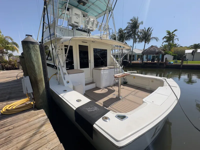 Slide: The Image of 1983 Bertram 46 Convertible yacht docked by a wooden pier, surrounded by palm trees. - 3