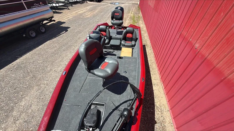 Slide: The Image of 2025 Tracker Pro Team 190 boat with red and gray seating, parked near a red building. - 2