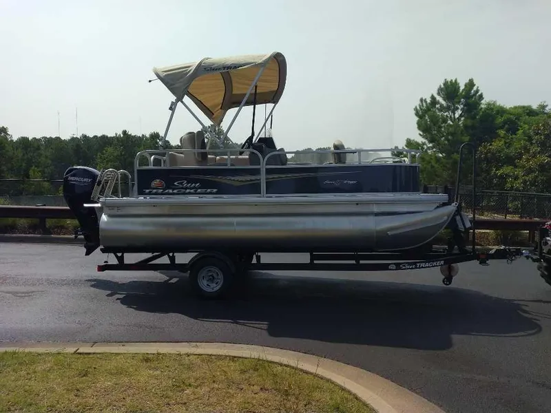 Slide: The Image of 2025 Sun Tracker Bass Buggy 16 XL Select pontoon boat on trailer, parked outdoors. - 5