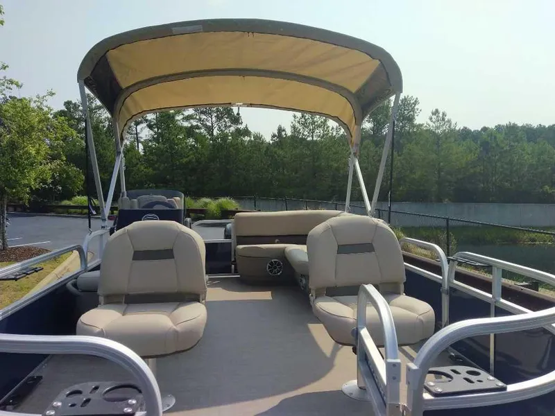 Slide: The Image of 2025 Sun Tracker Bass Buggy 16 XL Select pontoon boat with canopy and seating, docked near trees. - 7