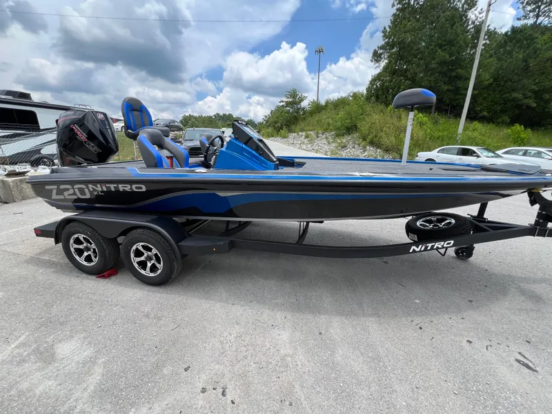 Slide: The Image of 2025 Nitro Z20 XL boat on trailer, blue and black design, parked outdoors. - 2