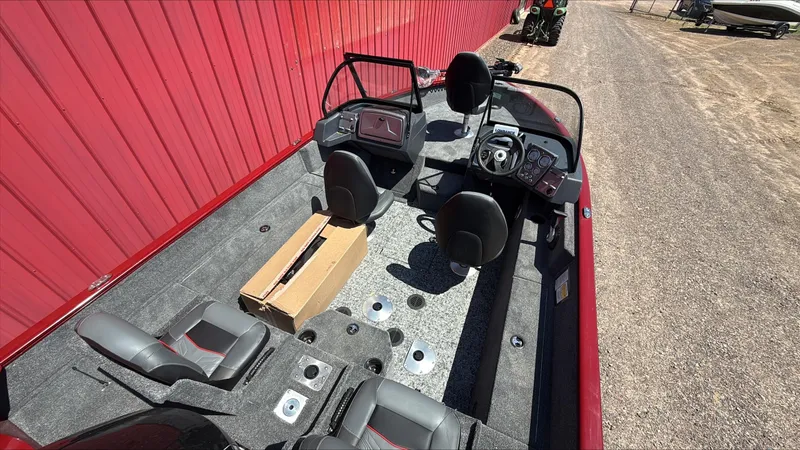 Slide: The Image of 2025 Tracker Pro Guide V-175 Combo boat interior with seating and controls, parked by a red wall. - 2