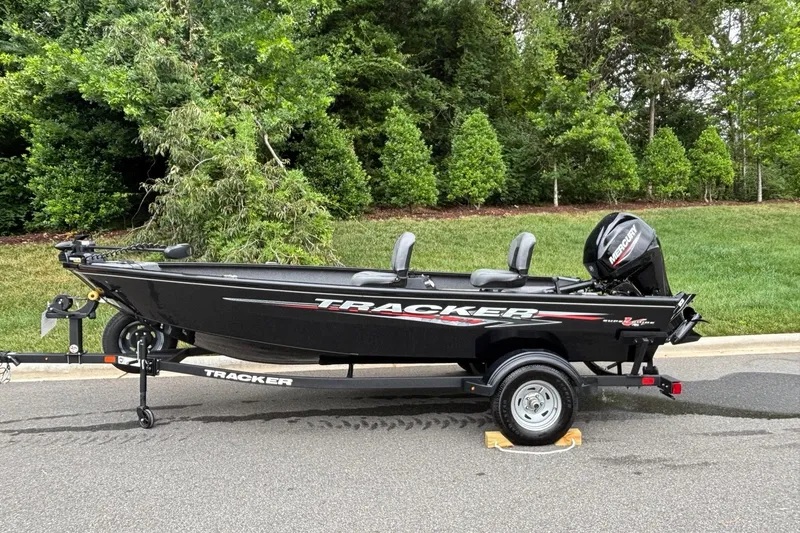 The Image of 2025 Tracker Super Guide V-16 T boat on trailer, parked on road with greenery background. - 0
