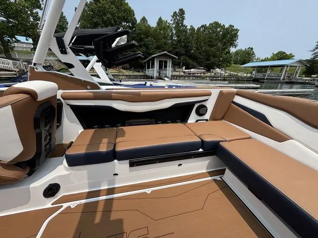 Slide: The Image of 2025 Axis Wake Research T235 boat interior with brown and white seating, docked by a lakeside. - 5
