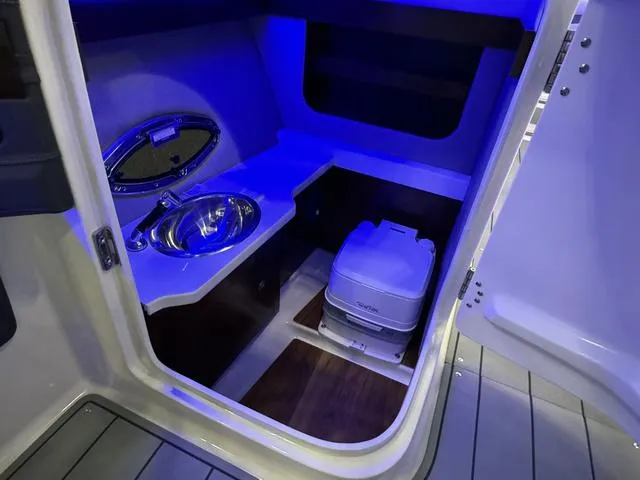 Slide: The Image of 2024 Chaparral 307 SSX boat interior with sink and portable toilet, illuminated by blue lighting. - 17