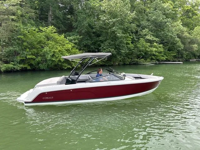 Slide: The Image of 2024 Cobalt CS23 boat cruising on a serene lake with lush green surroundings. - 1