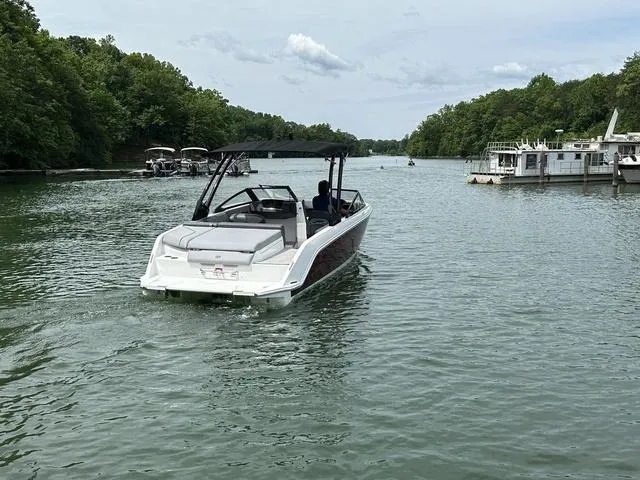 Slide: The Image of 2024 Cobalt CS23 boat cruising on a scenic lake with lush green surroundings. - 2