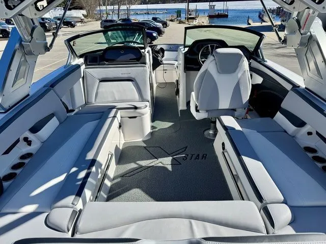 Slide: The Image of 2022 MasterCraft XStar boat interior with spacious seating and modern design, docked near a waterfront. - 14