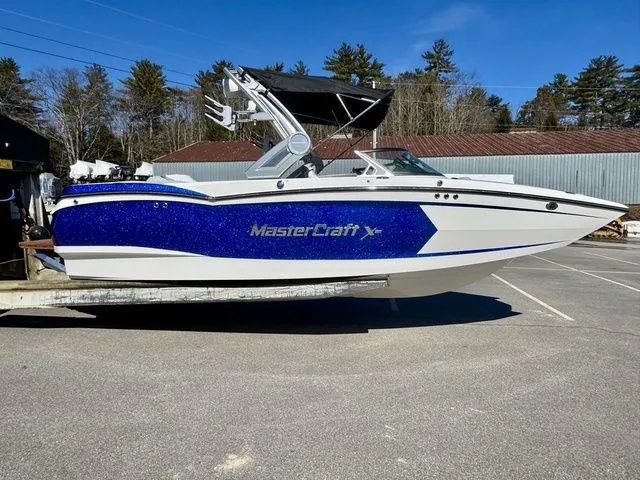 Slide: The Image of 2022 MasterCraft XStar boat with blue accents, parked outdoors on a sunny day. - 2