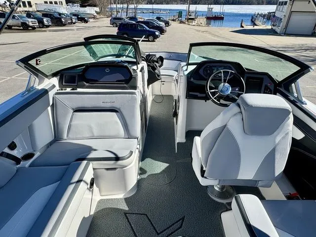 Slide: The Image of 2022 MasterCraft XStar boat interior with modern seating and dashboard, parked near a waterfront. - 21