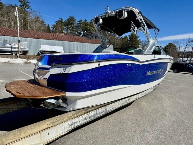 Slide: The Image of 2022 MasterCraft XStar boat with blue and white exterior, parked outdoors. - 3