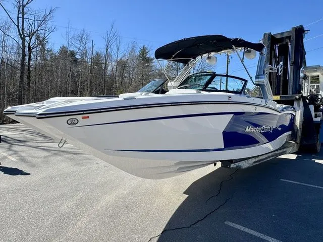 Slide: The Image of 2022 MasterCraft XStar boat on forklift, white and blue, parked outdoors. - 5